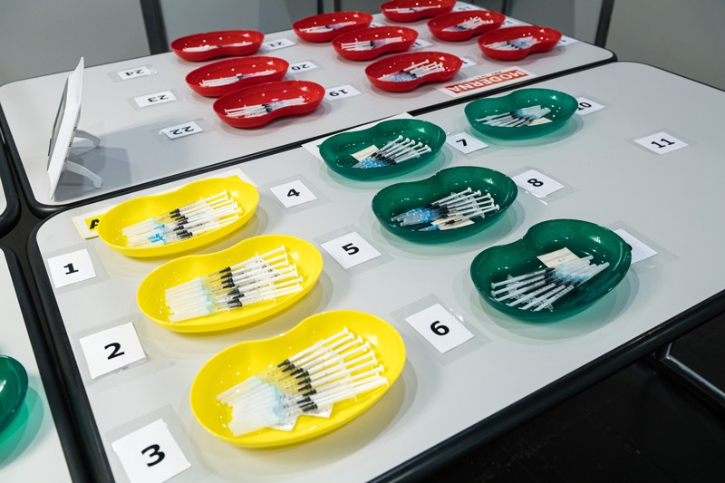 A table at a vaccination center covered in many different colored kidney dishes containing different kinds of COVID-19 vaccine