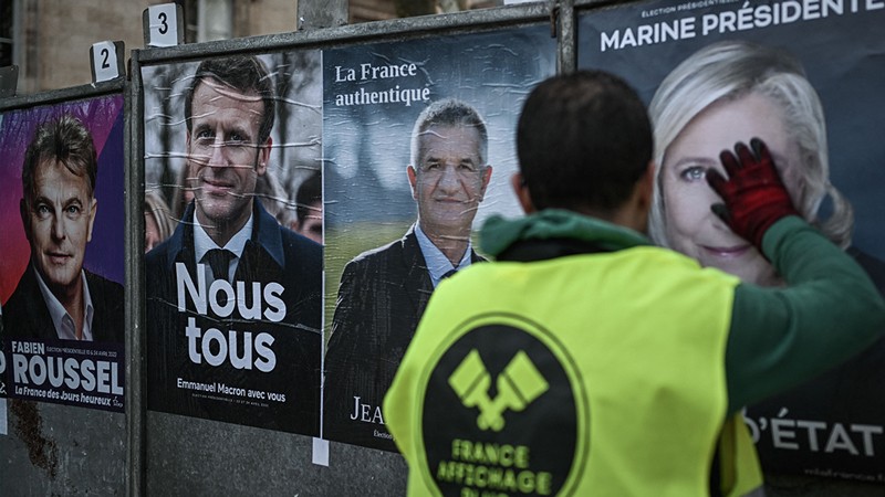 An employee of a display company placards presidential candidates' official campaign posters in France.