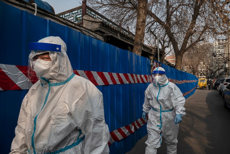 Workers wear protective suits as they walk along the fence of a barricaded community with high COVID-19 cases in Beijing
