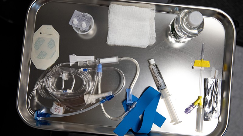 A metal tray holding a syringe, tube, pills and other medical equipment.