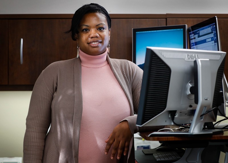 Cherisse Madlock-Brown poses for a portrait surrounded by computer monitors