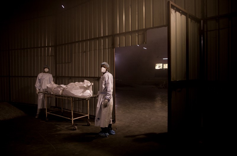 Workers in PPE move the body of a patient who died of the Covid-19 on a gurney through a dark warehouse