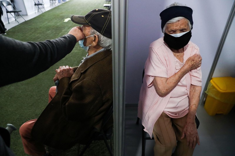 After receiving the flu vaccine, an elderly woman holds her arm and a man waits in the next chair
