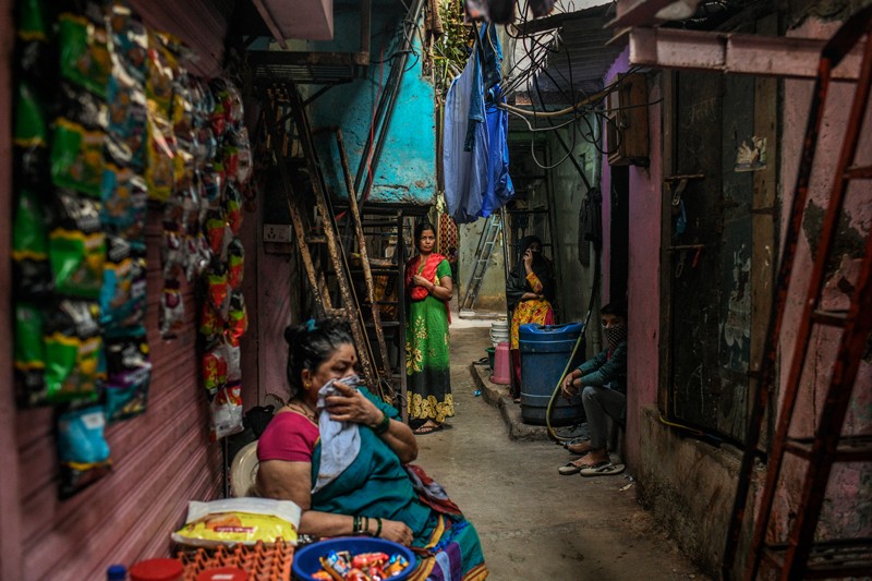 Residents, one of whom covers his mouth and nose with a cloth, sit in a narrow alley in Mumbai's Dharavi slum
