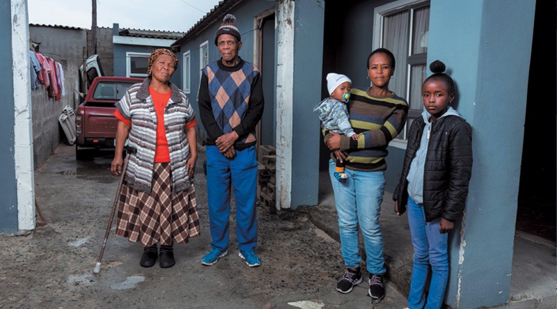 Four members of the Sityaya family, one of whom is carrying a baby, stand outside their house