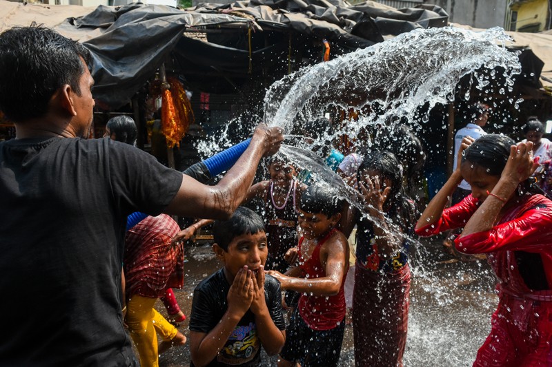 A man sprays water from a hose to cool down a group of children in India