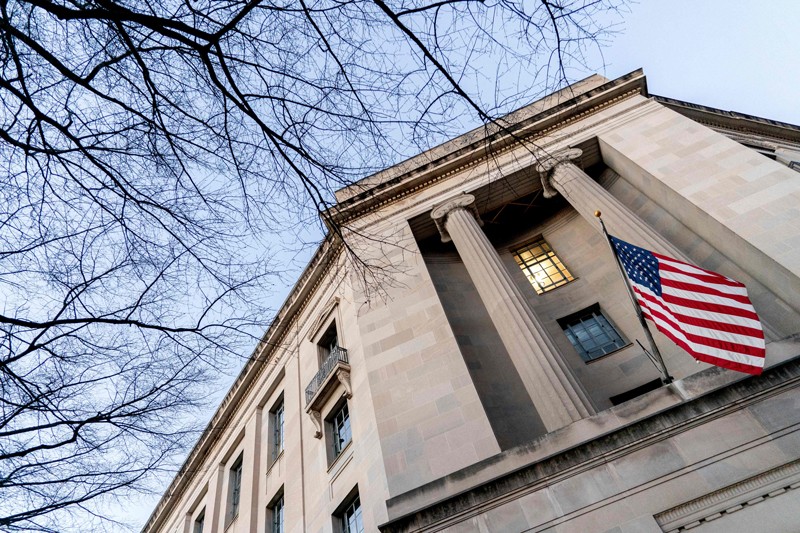 A low angle image looking up at the Department of Justice building with tree branches on the left side