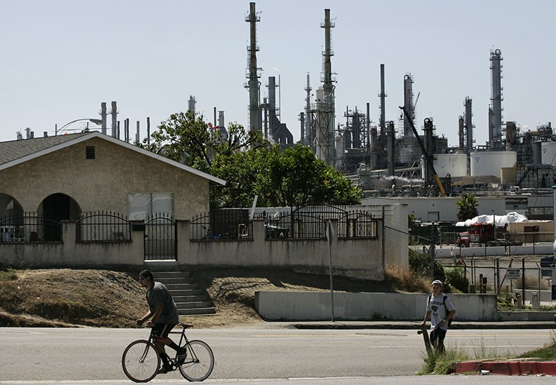 A person on a bike and a person on a skateboard in front of a home and a ConocoPhillips refinery in Los Angeles, California, US.