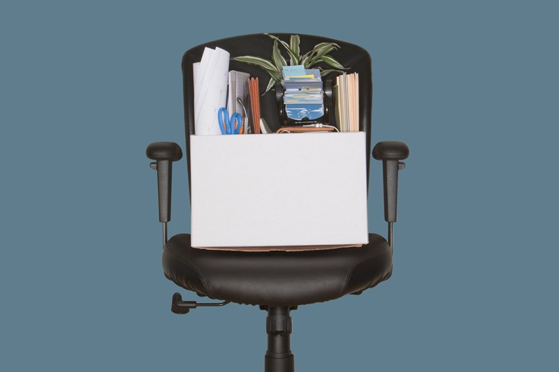 A black office chair with a cardboard box filled with files, office supplies and a pot plant balanced on the seat