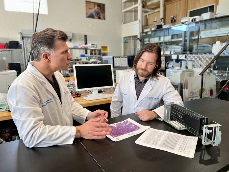 Charles Keller and Noah Berlow in discussion sitting at a lab bench in the Children's Cancer Therapy Development Institute labs