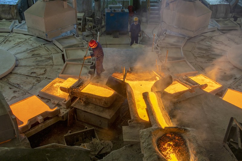 A person in heat protective gear and a red hardhat works as the copper flows into molds at a smelting plant in China.