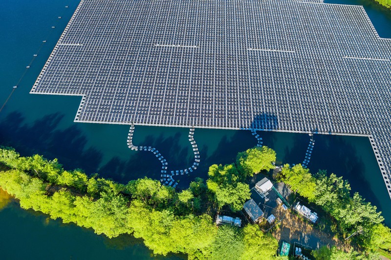 Panorama view of a water reservoir with floating solar panels leading to land under the sunlight.