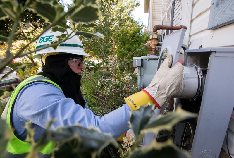 A worker wearing protective equipment installs a new Smart meter on the outside of a house