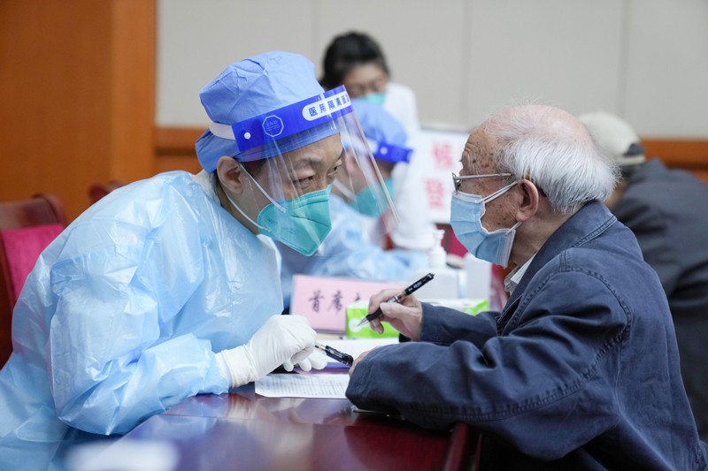 A medical worker wearing full PPE explains the content of a consent letter to an elderly man wearing a face mask