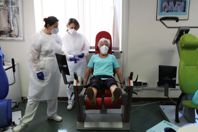 Een herstelde Coronavirus-patiënt zit in een oefenstoel terwijl hij wordt gecontroleerd door beroepsbeoefenaren in de gezondheidszorg