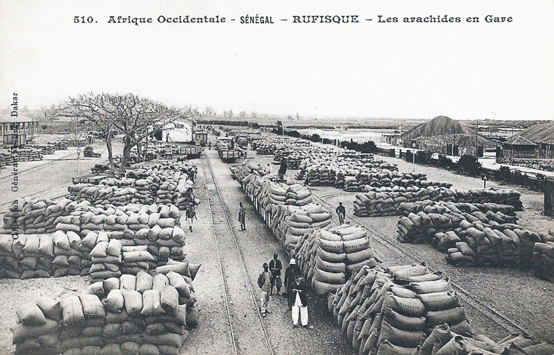 An old black and white image of rows of stacked bags of peanuts at a train station