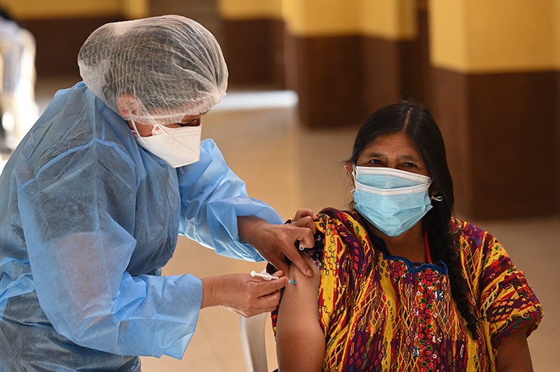 A masked woman is vaccination by a health worker in protective gear.