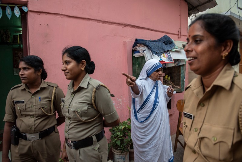 Three women in khaki uniforms walking down a street, past a nun in a blue and white habit.