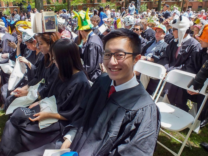 Jonathan Park is sitting down at graduation and surrounded by other people