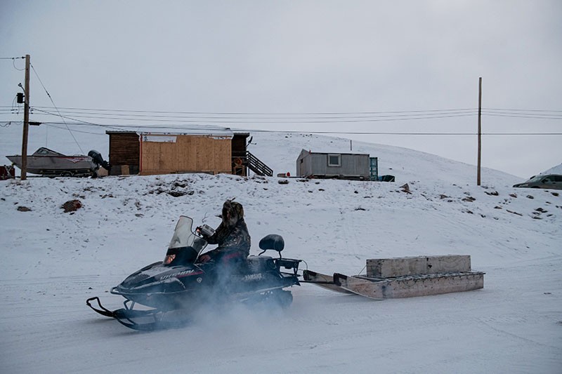 A scientist studying sea ice change drives a snowmobile along the beach in Pond Inlet, Nunavut, Canada.