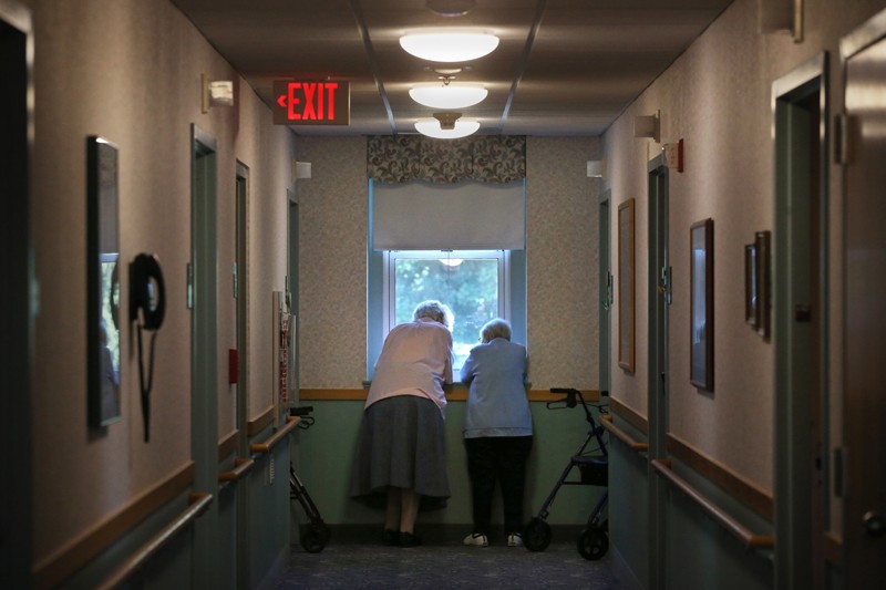 Two elderly women lean against a windowsill while having a chat in their retirement home