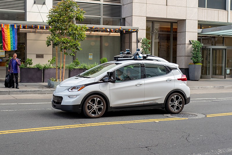 Light grey car in the street with machinery attached to its roof and sides to enable self-driving