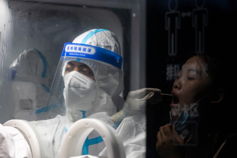 A reflection shows a woman getting a COVID-19 test at a testing station by a worker in full PPE
