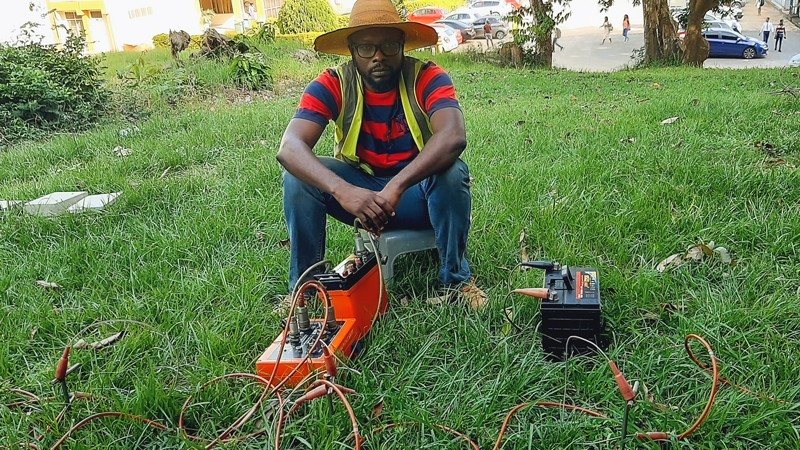 Cyril sits on a stool while conducting a resistivity survey