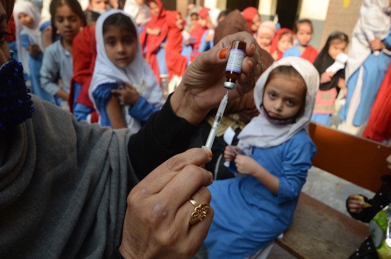 A health worker holds up a dose of a vaccine in front of a group of young children