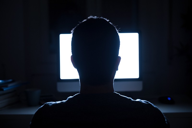 Silhouette of man's head in front of computer monitor light at night.