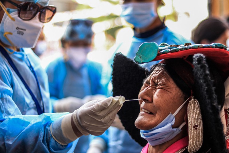Una mujer con un tocado tradicional frunce el ceño mientras un trabajador de la salud se limpia la nariz como parte de una prueba de detección de COVID-19 en India.