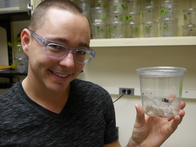 Jonathan Pruitt sosteniendo un recipiente de plástico transparente que contiene una araña