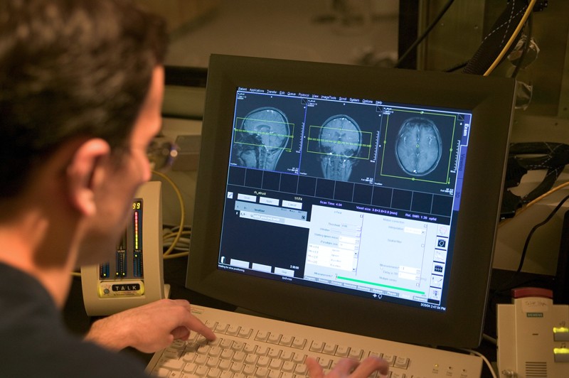 A researcher inputs data into a computer in the control room of a fMRI scanner