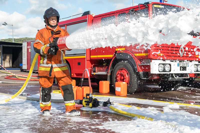 A firefighter holds a foam dispenser while spraying foam in front of a fire truck