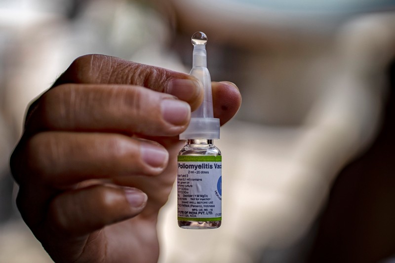 A community health worker holds up a vial of an oral polio vaccine.