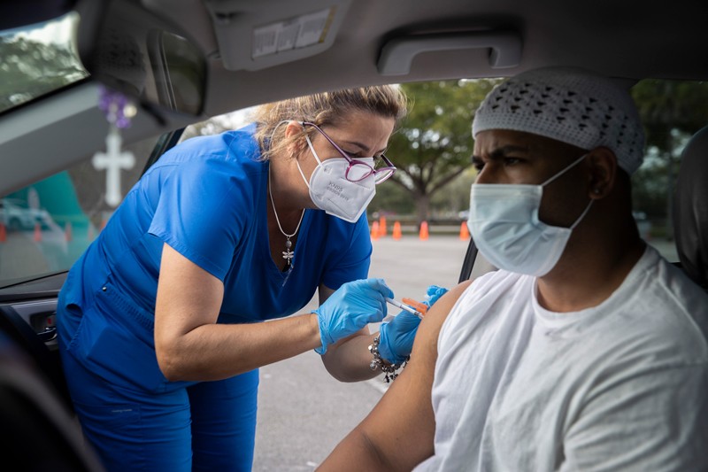 A man wearing a mask receives a covid vaccine from a medical worker in his car