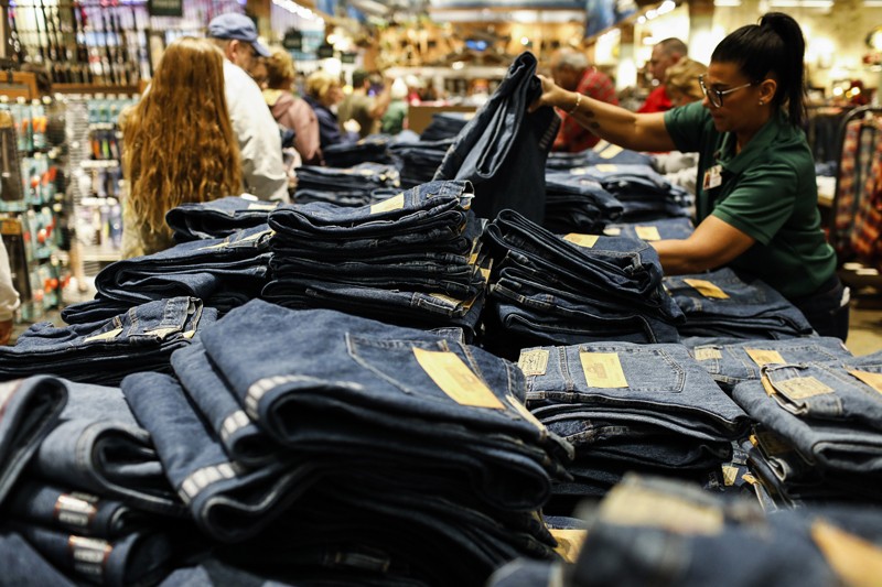 A retail employee arranges jeans displayed for sale on a table
