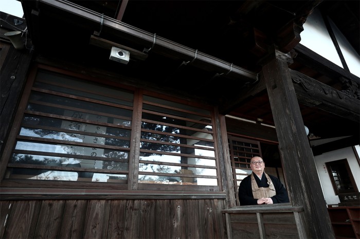 A priest smiles at the camera from his Buddhist temple. A small geiger counter is attached to the underside of roof at top left.