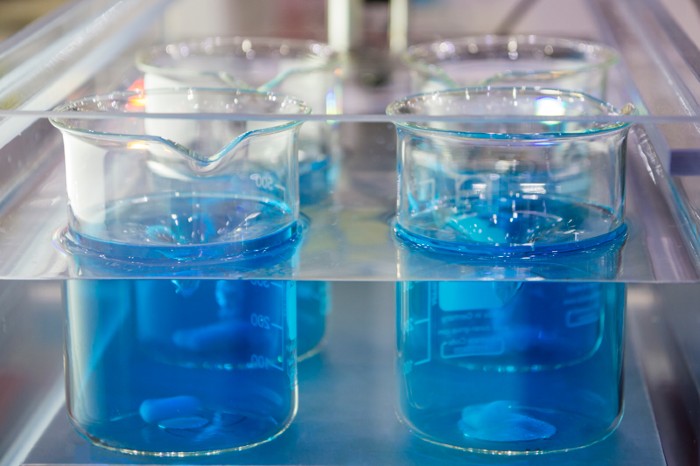Four beakers containing blue liquid and spinning magnetic stirrer bars in a lab