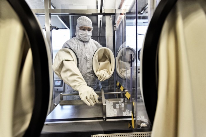 A technician in a protective suit uses a glove box to handle vaccine vials