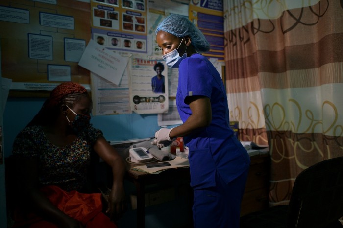A female nurse wearing a gloves and a surgical mask tends to a patient at health care centre in Nairobi, Kenya