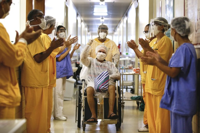 A man raises a fist in the air as he is pushed in a wheelchair down a hospital hallway lined with applauding workers in scrubs