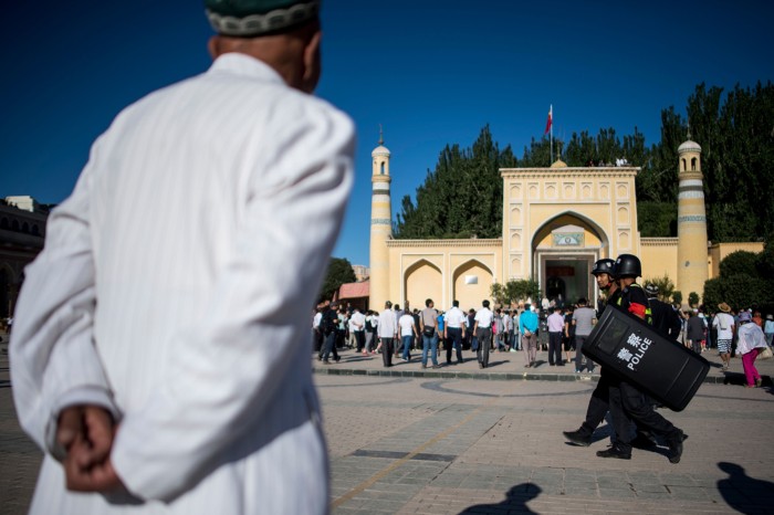 Police with helmets and riot shields walk through a crowd of men arriving at a mosque in Kashgar, Xinjiang, China