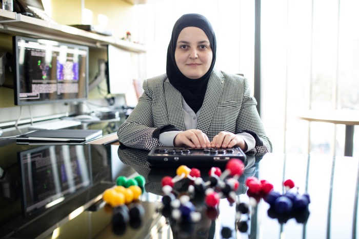 Mona Minkara sitting at a desk in her office. On the desk is a 3D textured Molecular Modelling kit and a braille notetaker