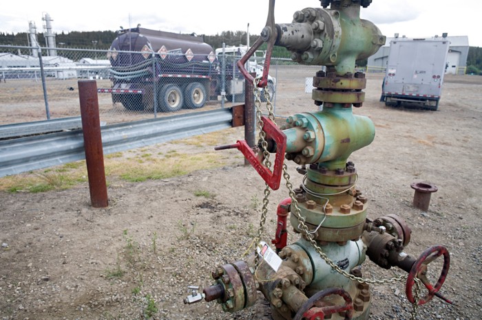 A chained up natural gas wellhead near a gas tanker truck and lorry