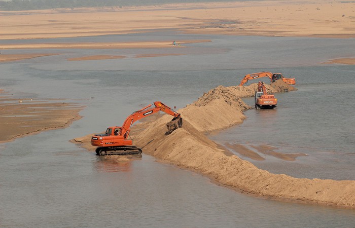 Laborers and machines work inside the Kuakhai river digging sand to transport to the area construction sites in India.