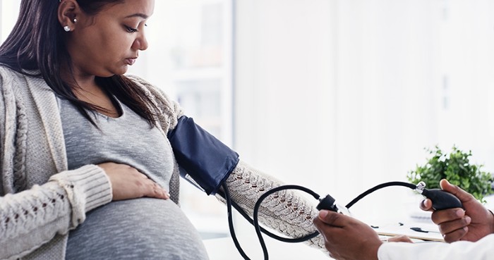 A pregnant woman getting her blood pressure checked by a doctor at a health care facility.