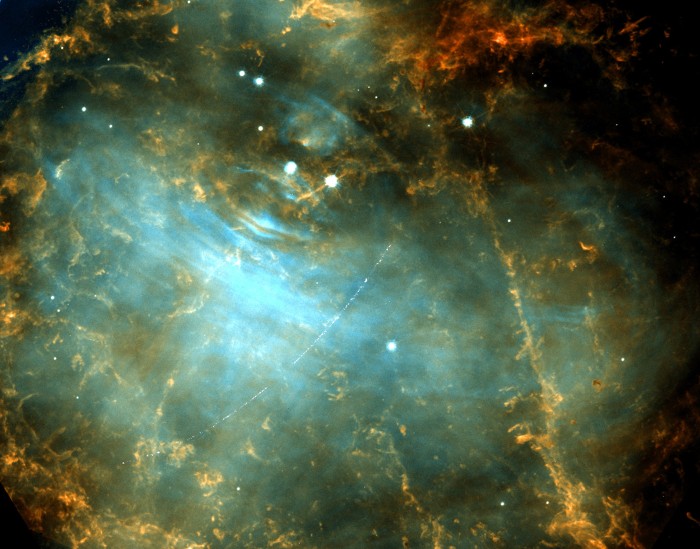 The Crab Nebula shown in green, blue and orange swirls, with a pale trail passing across it.