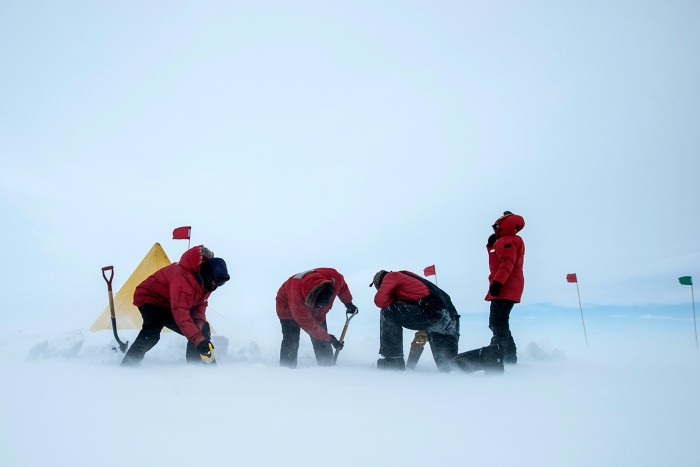 Four researchers in winter gear set up a Scott Tent on the Ross Ice Shelf, Antarctica, in high winds.