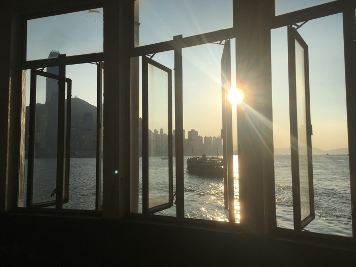 A cityscape by the sea is seen through a window with sunlight shining in